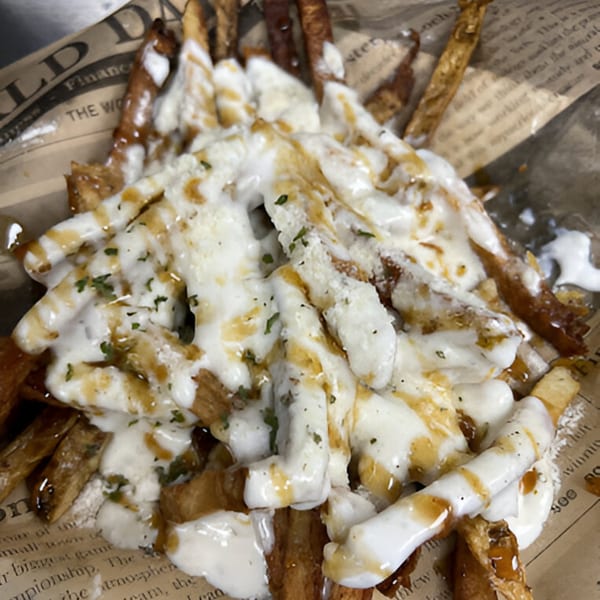 Close-up of golden french fries topped with melted white cheese, brown gravy, and green herbs.