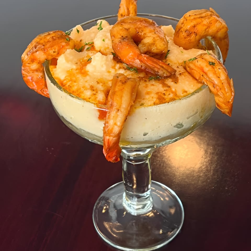 Shrimp and grits in a martini glass, garnished with parsley, on a dark wooden table.