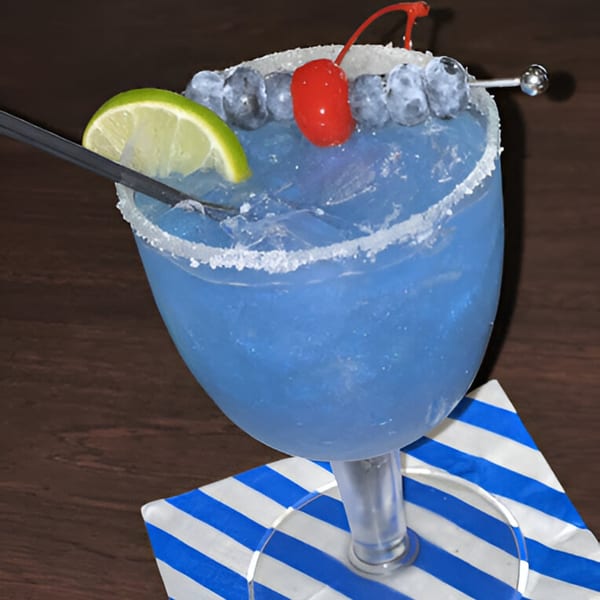 Blue cocktail with lime, blueberries, and a cherry, served on a striped napkin.