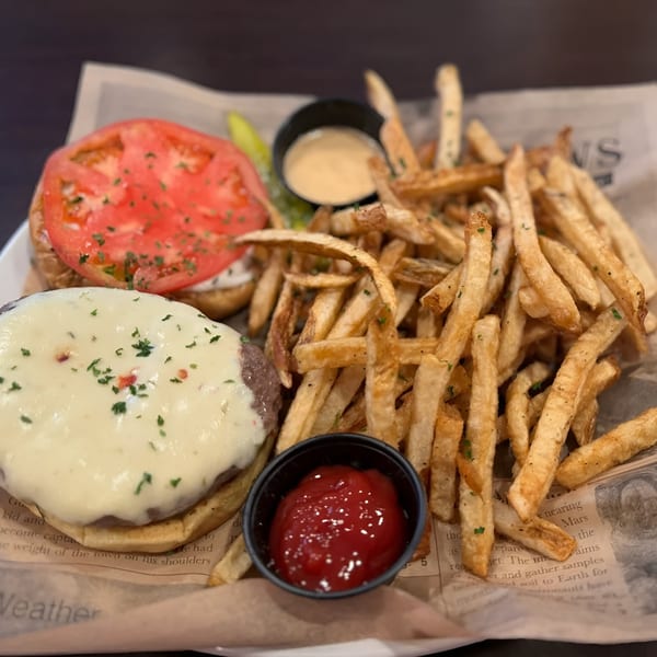 A Tulunes In The City burger with melted cheese and tomato, served with fries and ketchup.