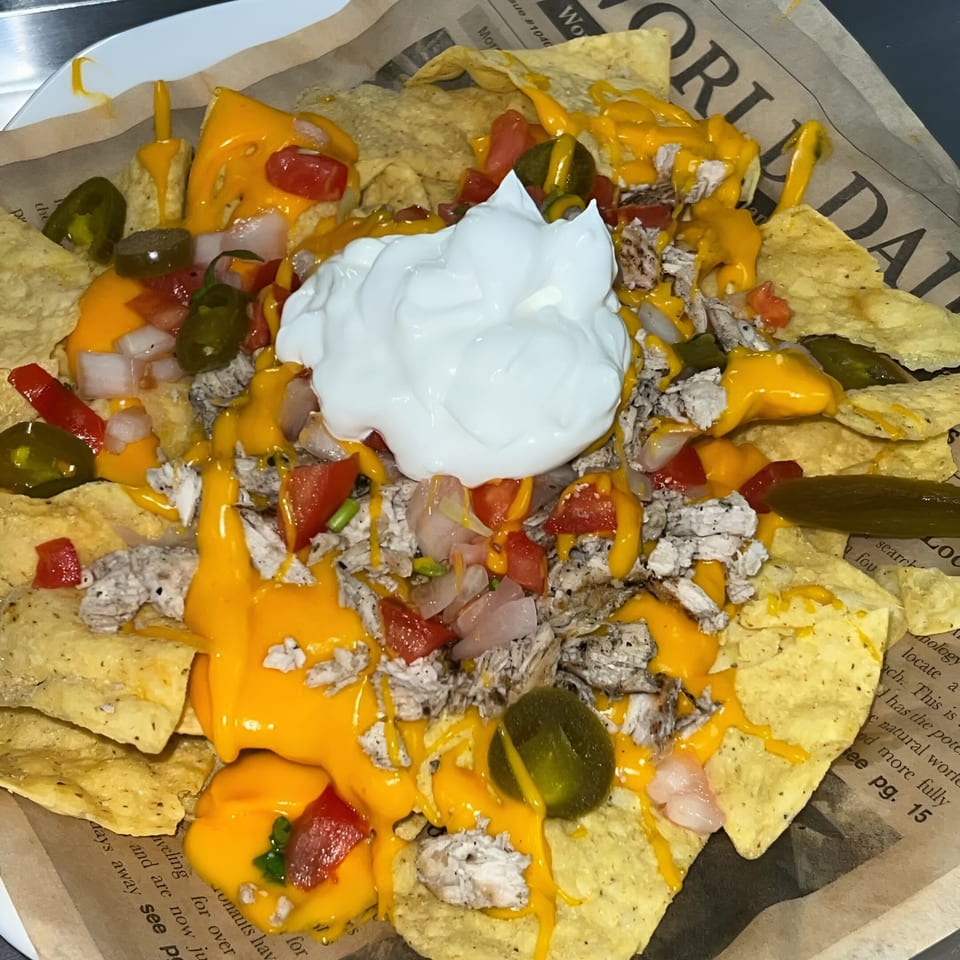 Chicken nachos with melted cheese, diced tomatoes, onions, jalapeños, and a dollop of sour cream.