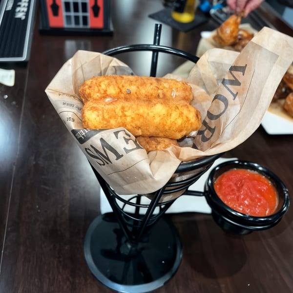 Golden-brown mozzarella sticks in a metal basket with a side of red marinara sauce.