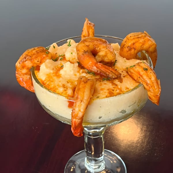 Shrimp and grits in a martini glass, garnished with parsley and paprika, on a dark table.