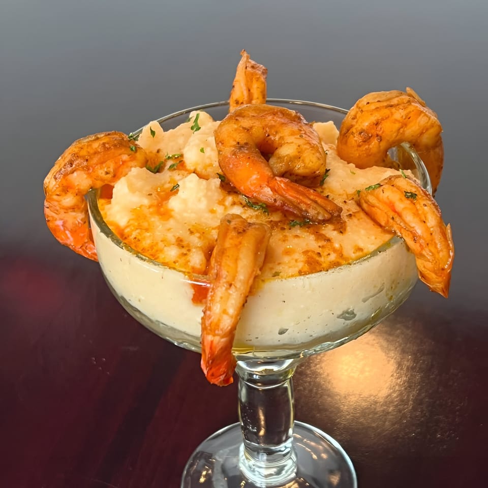 Shrimp and grits in a martini glass, garnished with parsley and paprika, on a dark table.